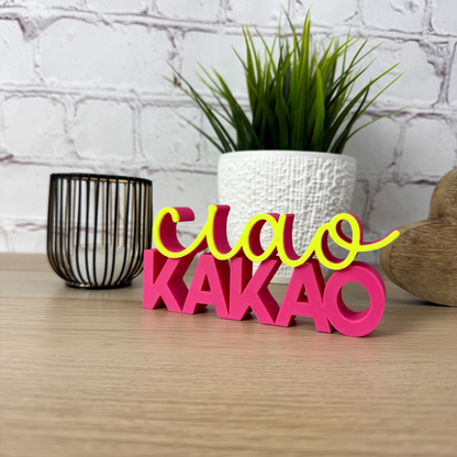 Bunter 3D-Schriftzug 'ciao kakao' in leuchtendem Pink und Gelb auf Holzuntergrund mit Dekoelementen