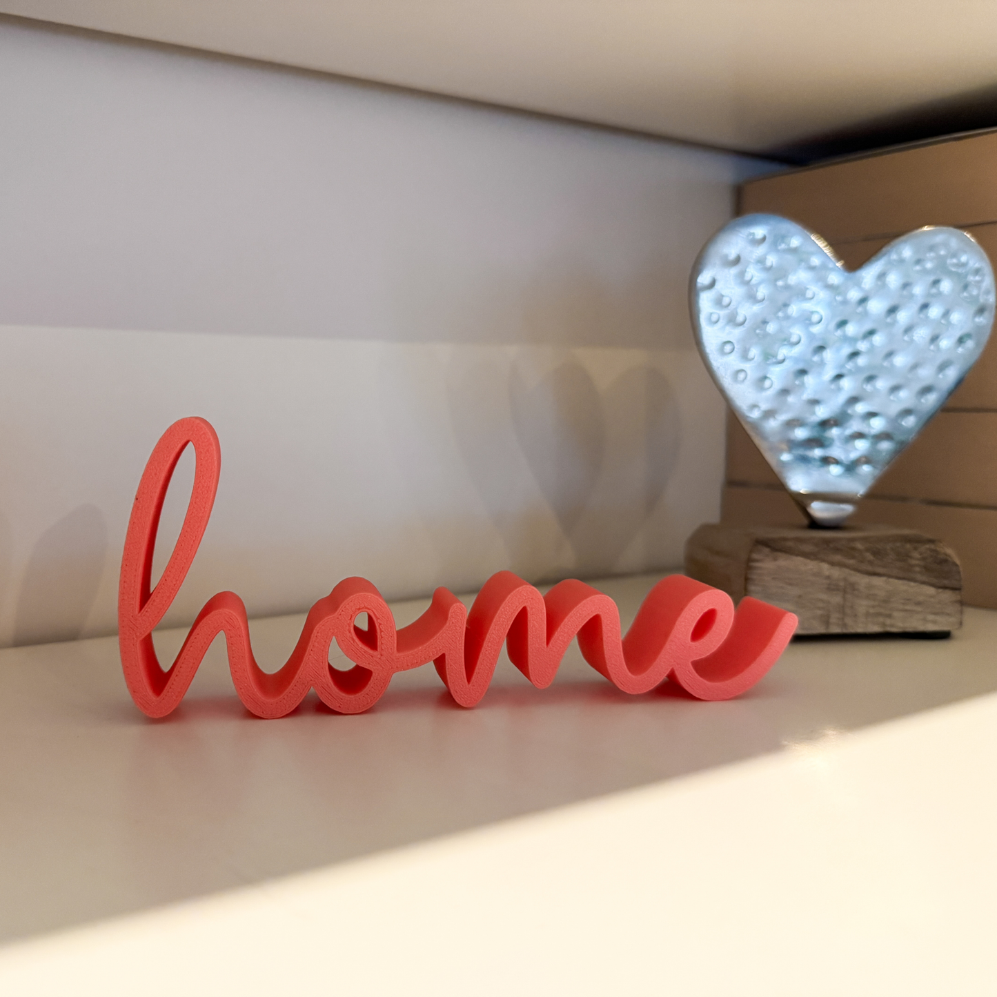 Schriftzug 'home' aus PLA+ in Regal mit Dekoherz – liebevolle Geschenkidee zum Einzug oder Geburtstag.