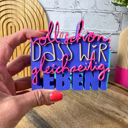 3D Spruch „Voll schön, dass wir gleichzeitig leben“ in lila, beige und magenta als Schild