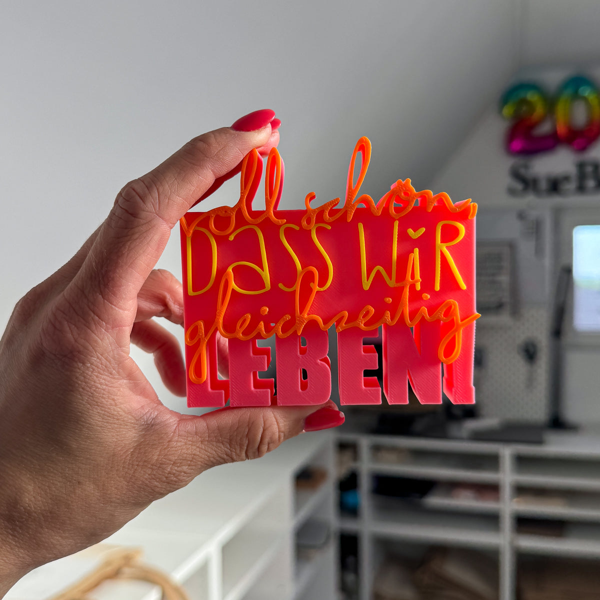 3D Spruch „Voll schön, dass wir gleichzeitig leben“ in Rosa, Orange und Gelb, Nahaufnahme in der Hand