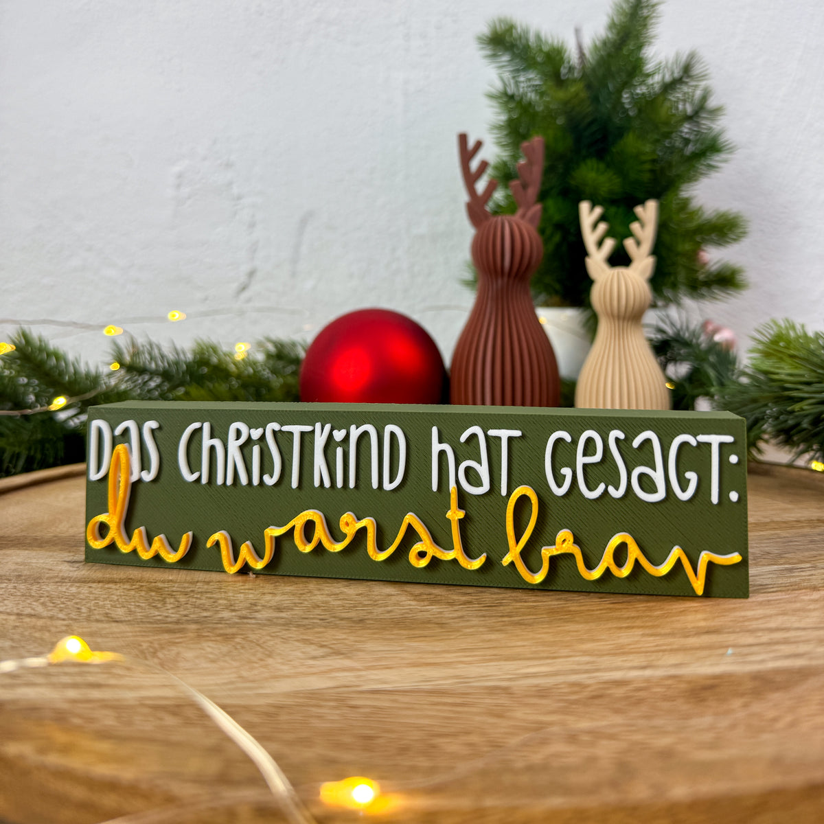 Weihnachtsdeko zum Hinstellen mit Christkind-Spruch in Weiß und Gold auf olivgrünem Schild, Rentierfiguren im Hintergrund