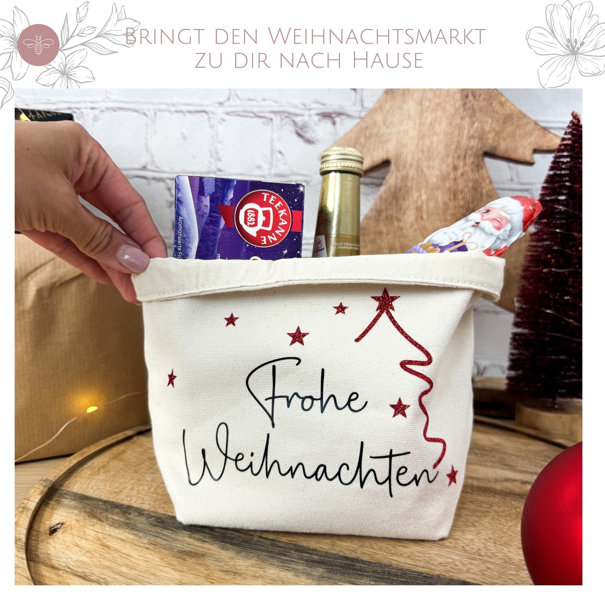 Hand hält einen Geschenkkorb „Frohe Weihnachten“, gefüllt mit Tee, Sekt und einem Schokoladen-Weihnachtsmann. Ein liebevolles Mitbringsel zu Weihnachten.