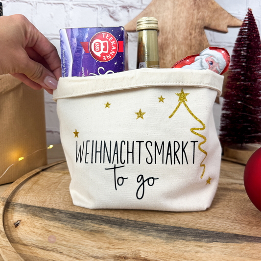 Hand hält einen Geschenkkorb "Weihnachtsmarkt to go", gefüllt mit Tee und einer Sektflasche. Ideales kleines Mitbringsel zu Weihnachten.