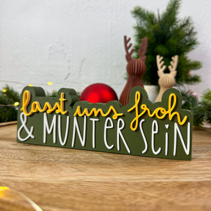 Weihnachtsspruch „Lasst uns froh und munter sein" auf dunkelgrünem Riegel mit Rentierfiguren