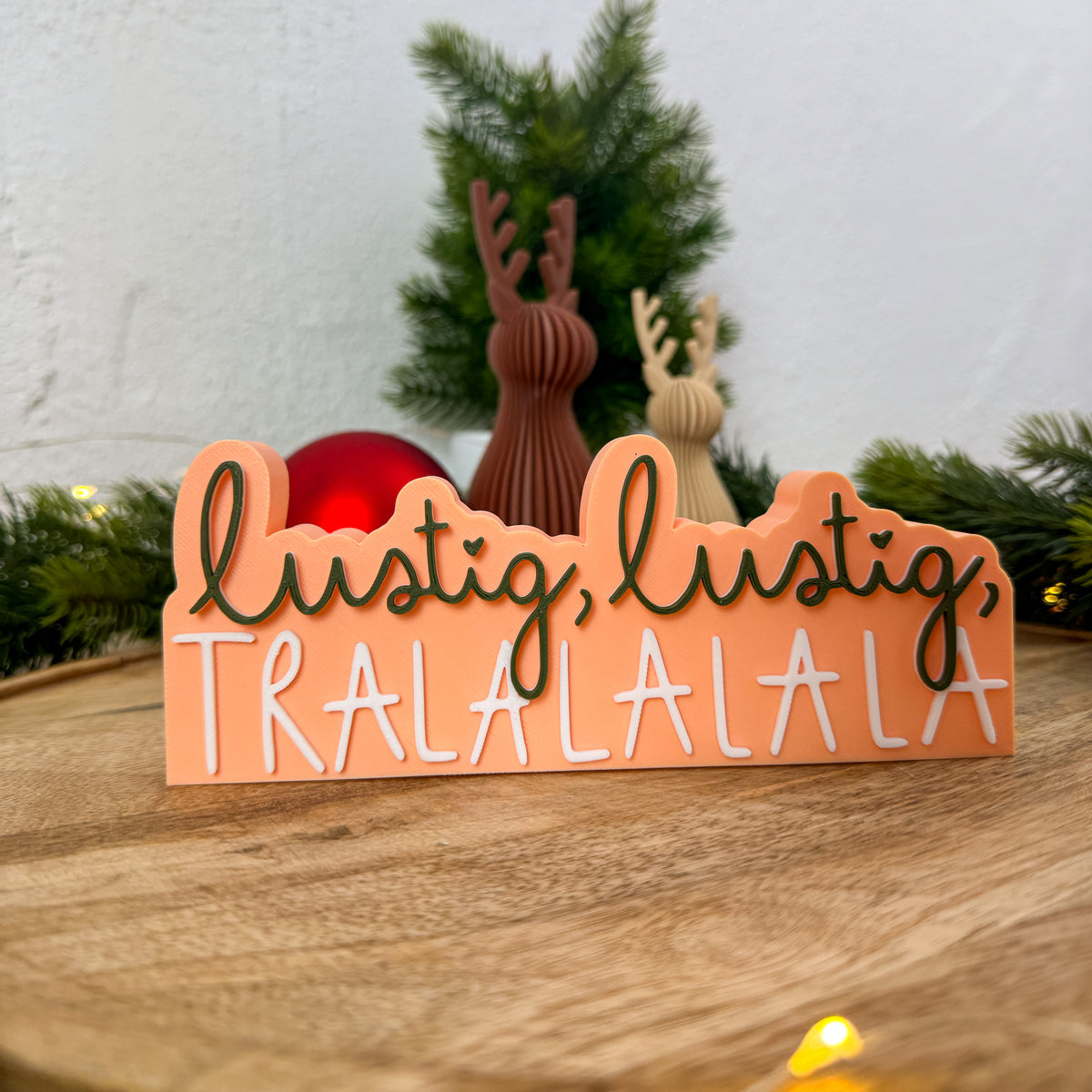 Weihnachtsspruch „lustig, lustig, TRALALALA" auf apricotfarbenem Schild mit Rentierfiguren