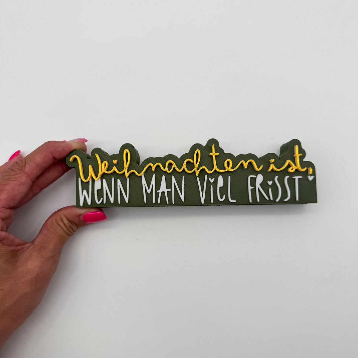 Schild „Weihnachten ist, wenn man viel frisst" in einer Hand gehalten vor weißem Hintergrund