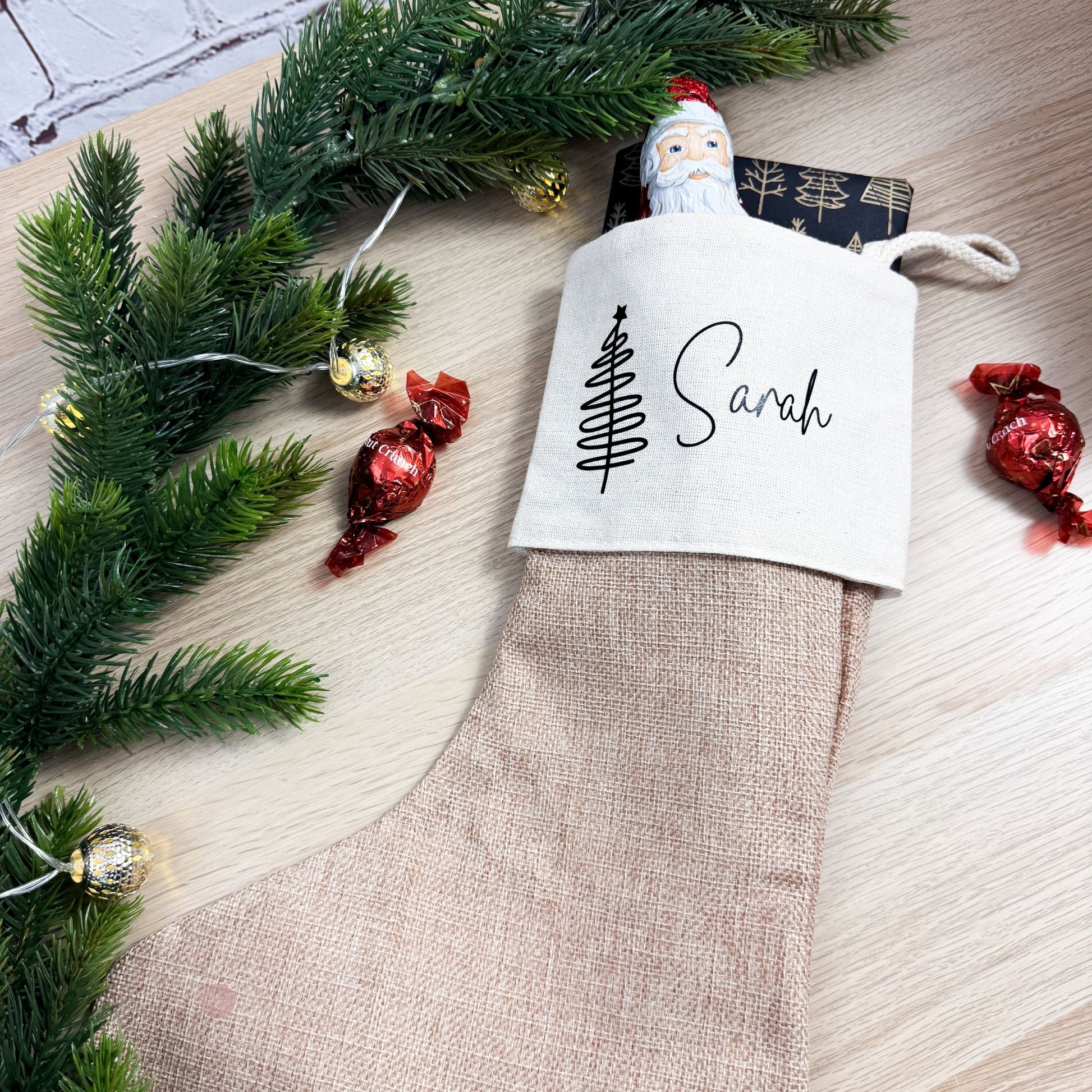 Nikolausstrumpf aus Jute mit Namensaufdruck Sarah und Geschenken – weihnachtlich dekoriert mit Tannenzweigen und Schokolade.